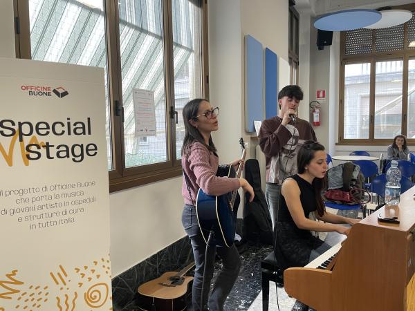 Giovani artisti si esibiscono dal vivo durante Special Stage di Officine Buone davanti a pazienti e caregiver in un ospedale.